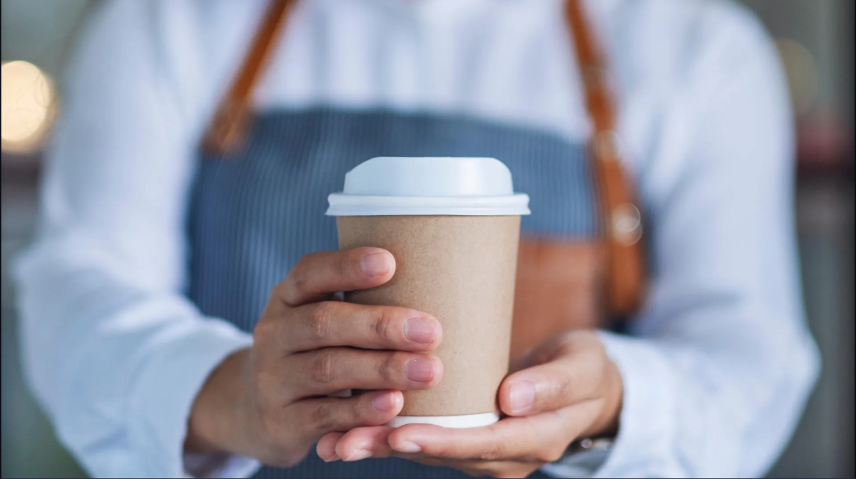Egy férfi fedeles, eldobható kávéspoharat tart